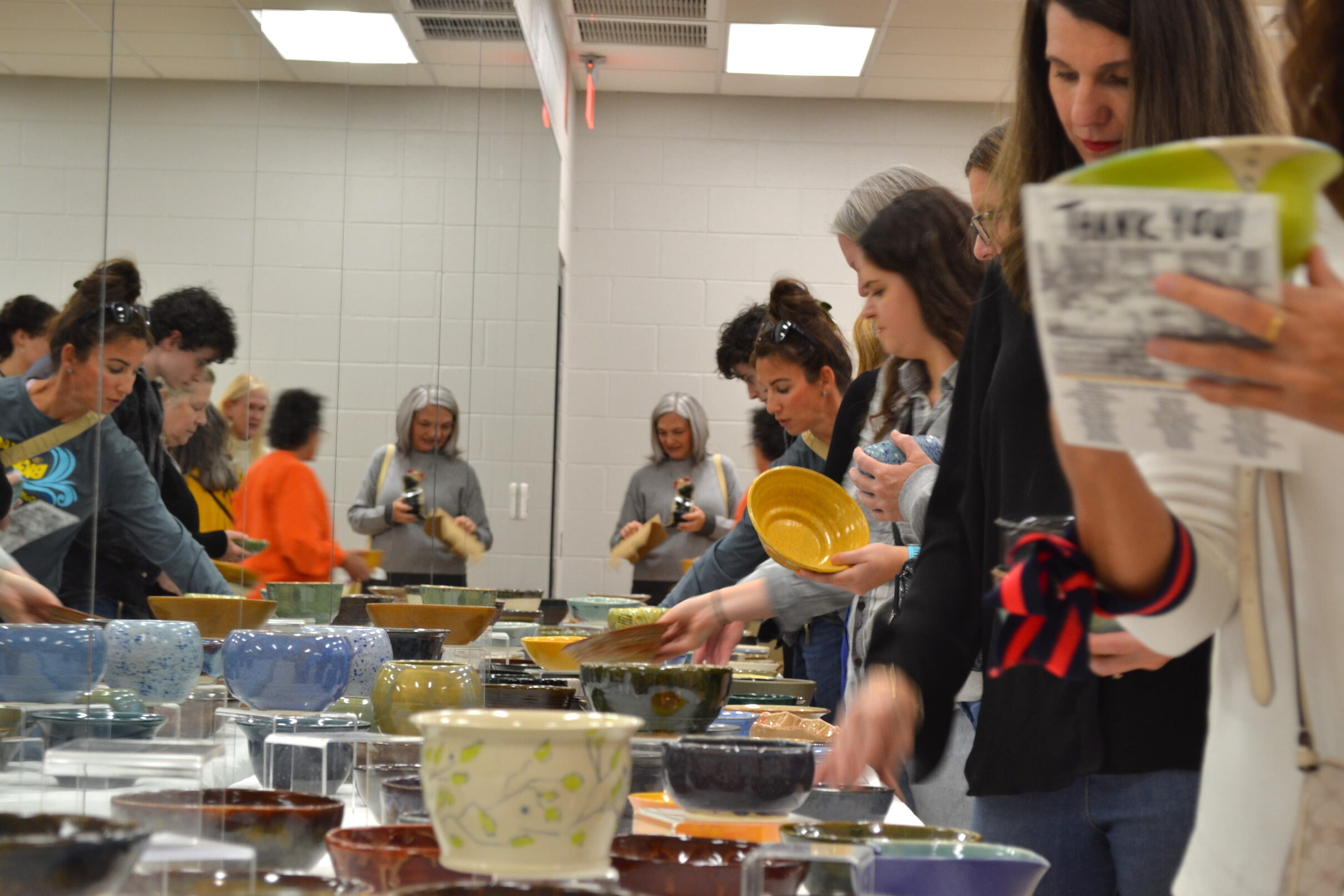 Image shows about 20 people looking at Empty Bowls on a large table