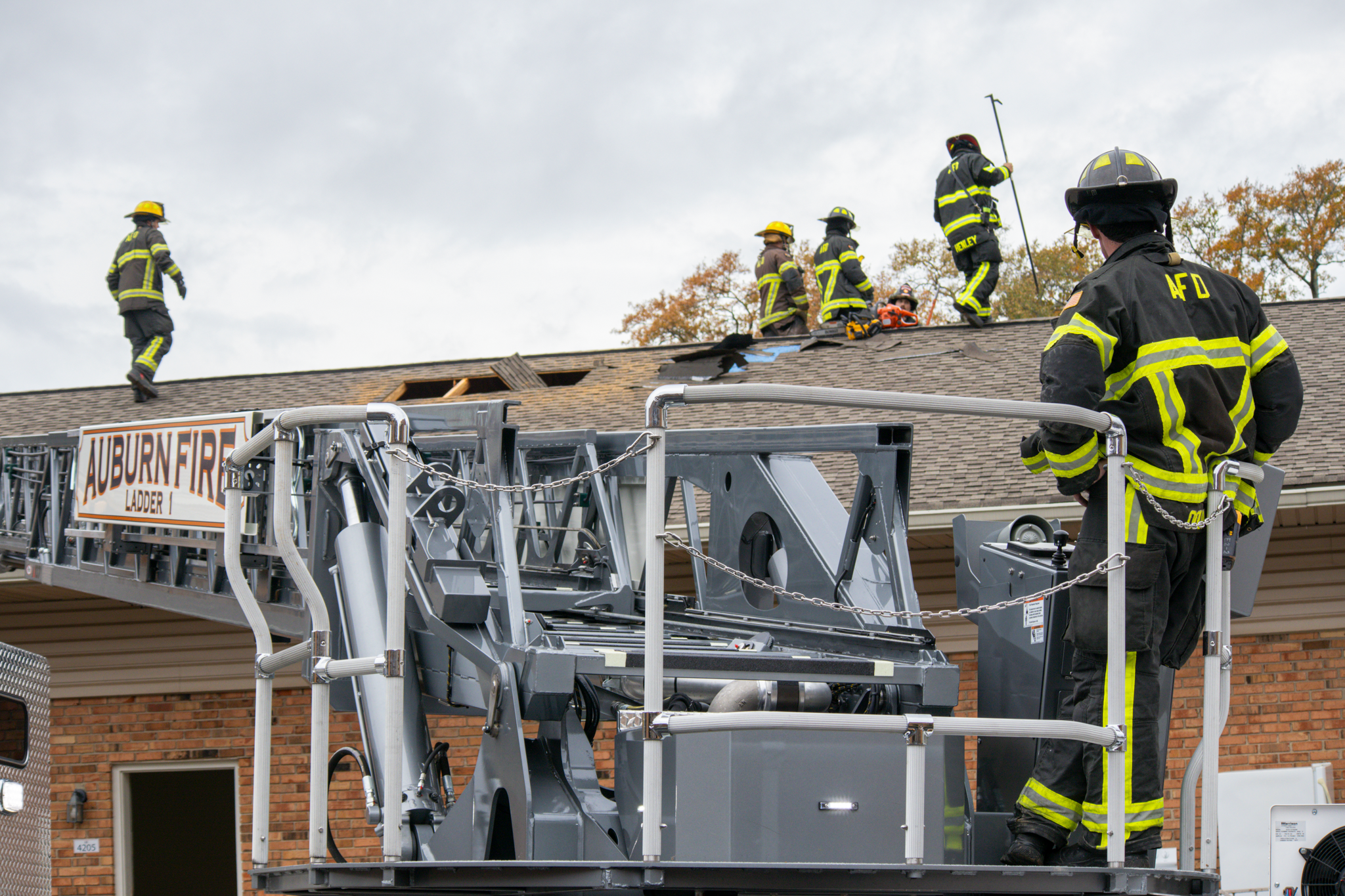 Firefighter on ladder watching other firefighters work on roof