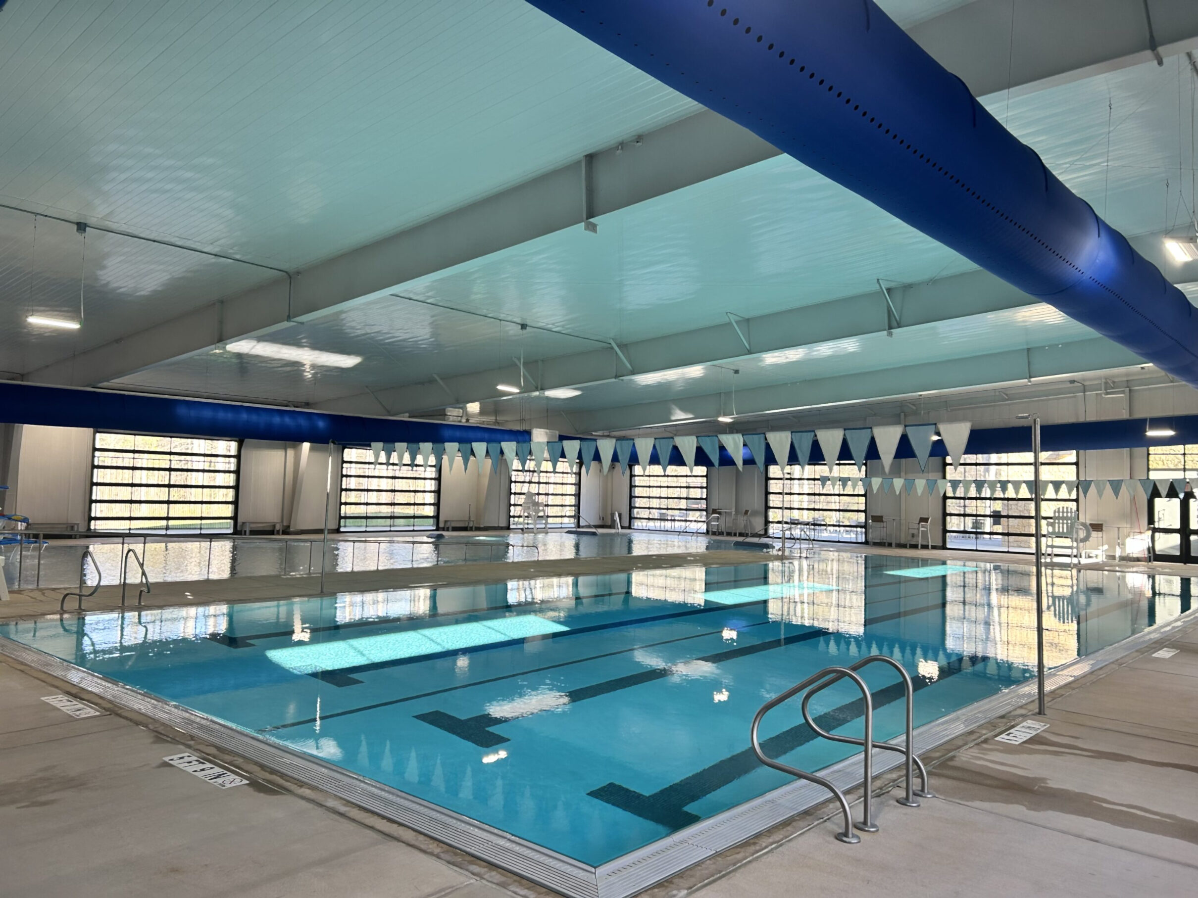 Indoor swimming pool with lap lanes, seating, and overhead lane flags.