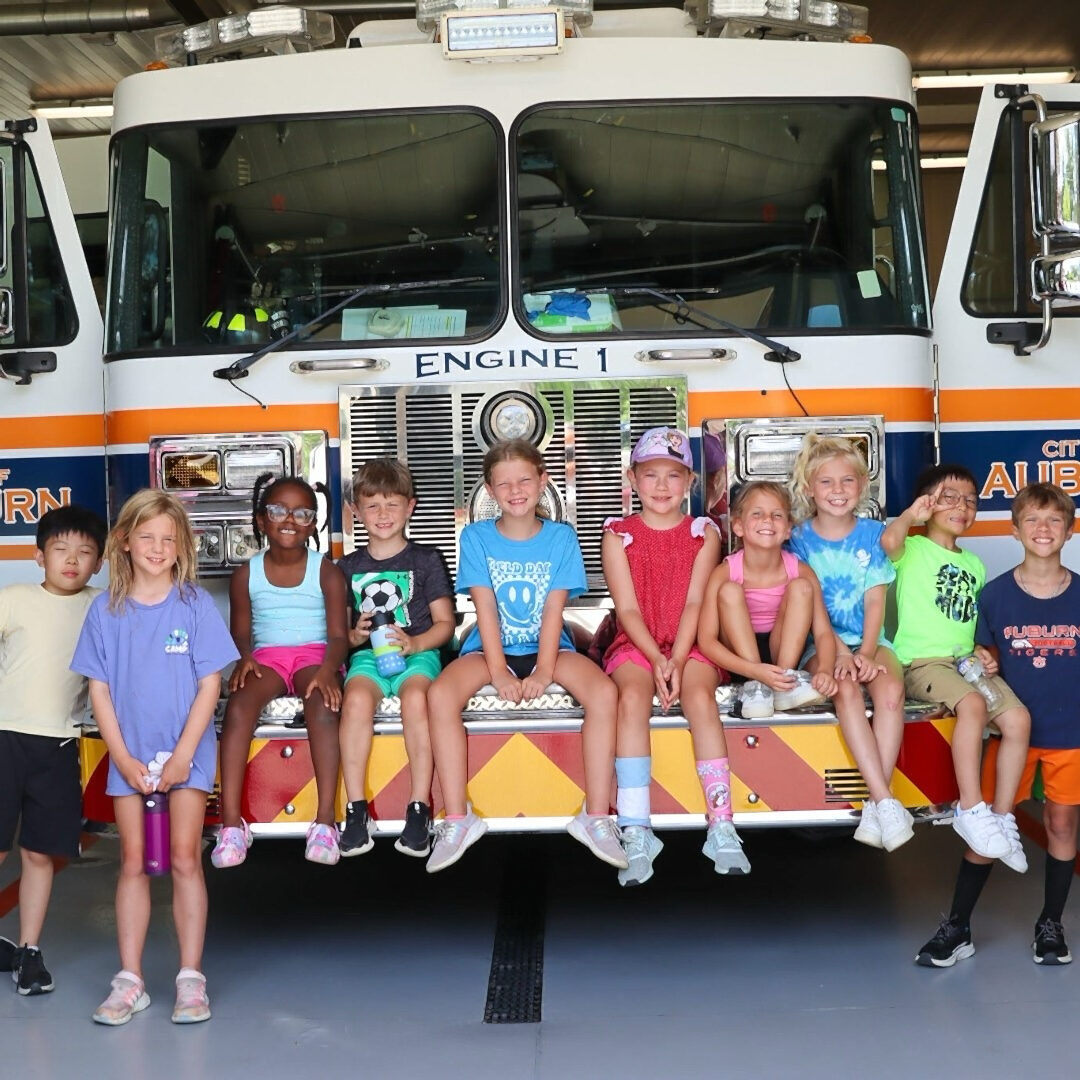A group of children seated on the front of a firetruck engine.