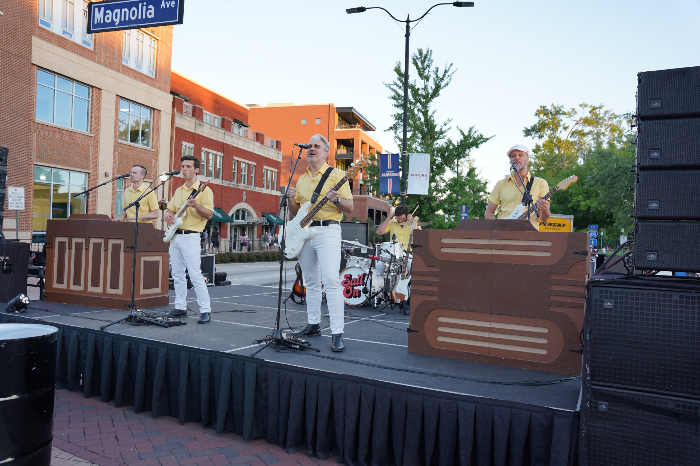 Image shows a band in yellow shirts holding their instsrumetns and singing