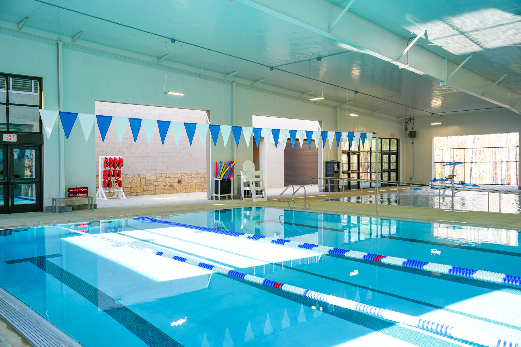 Indoor swimming pool with lap lanes, starting flags overhead, and bright natural light entering through windows.