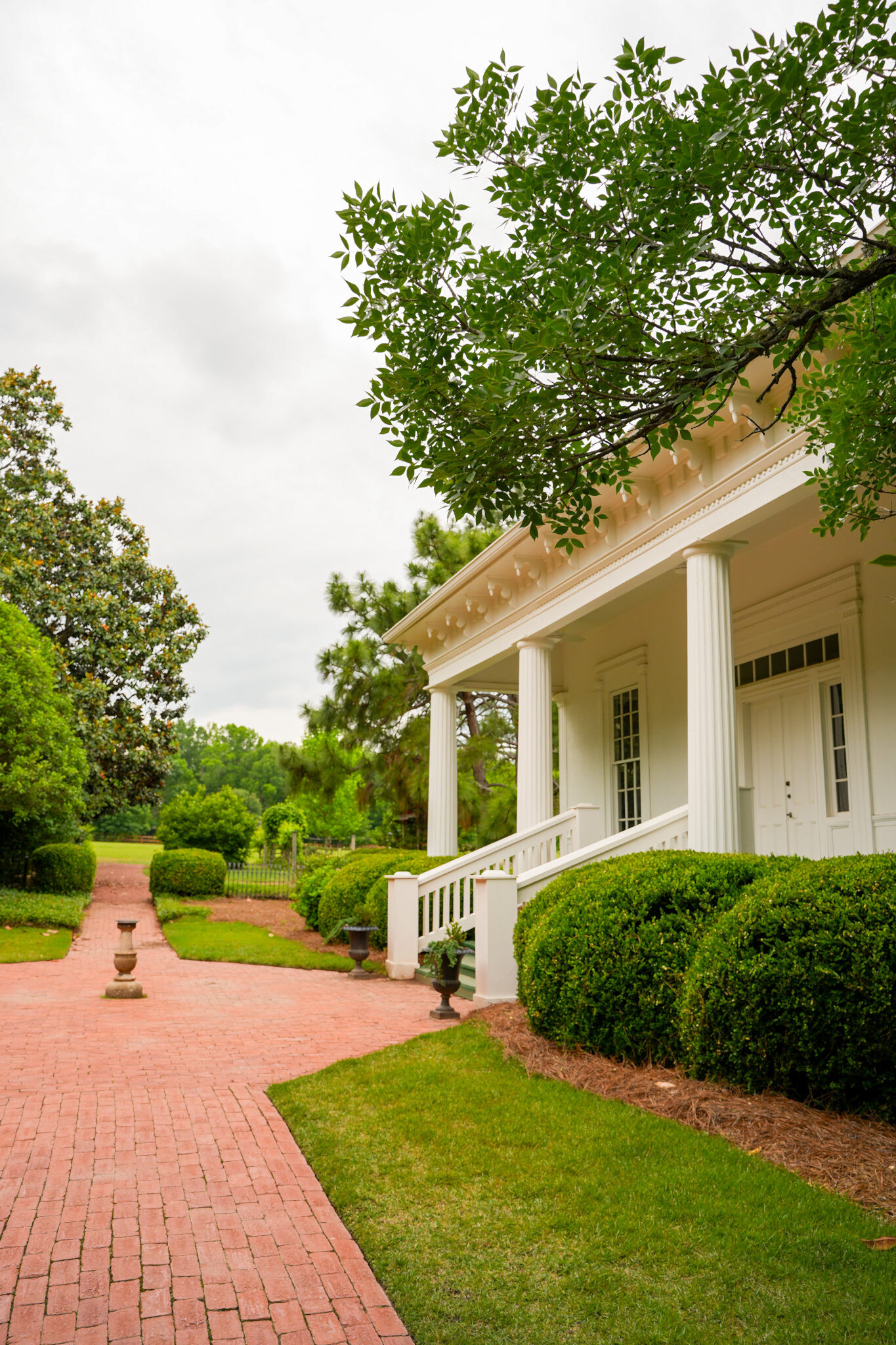 Brick walkway leading to a white columned building, surrounded by manicured landscaping and trees.