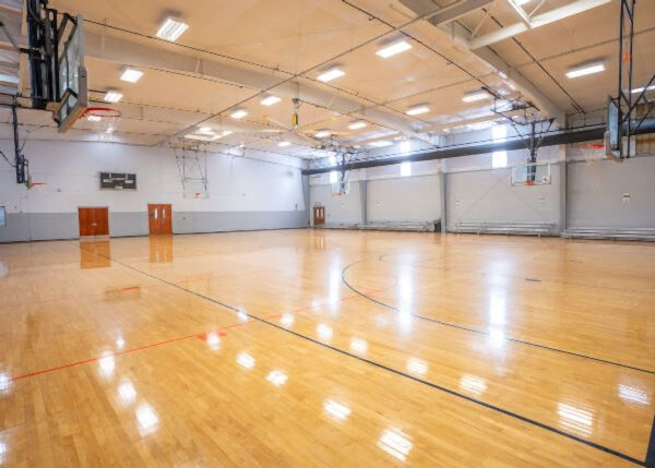 An indoor gymnasium with a polished wood floor, basketball hoops, and overhead lighting.