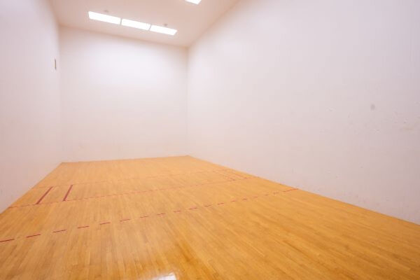 An indoor racquetball court with a wood floor, white walls, and red boundary lines under overhead lighting.