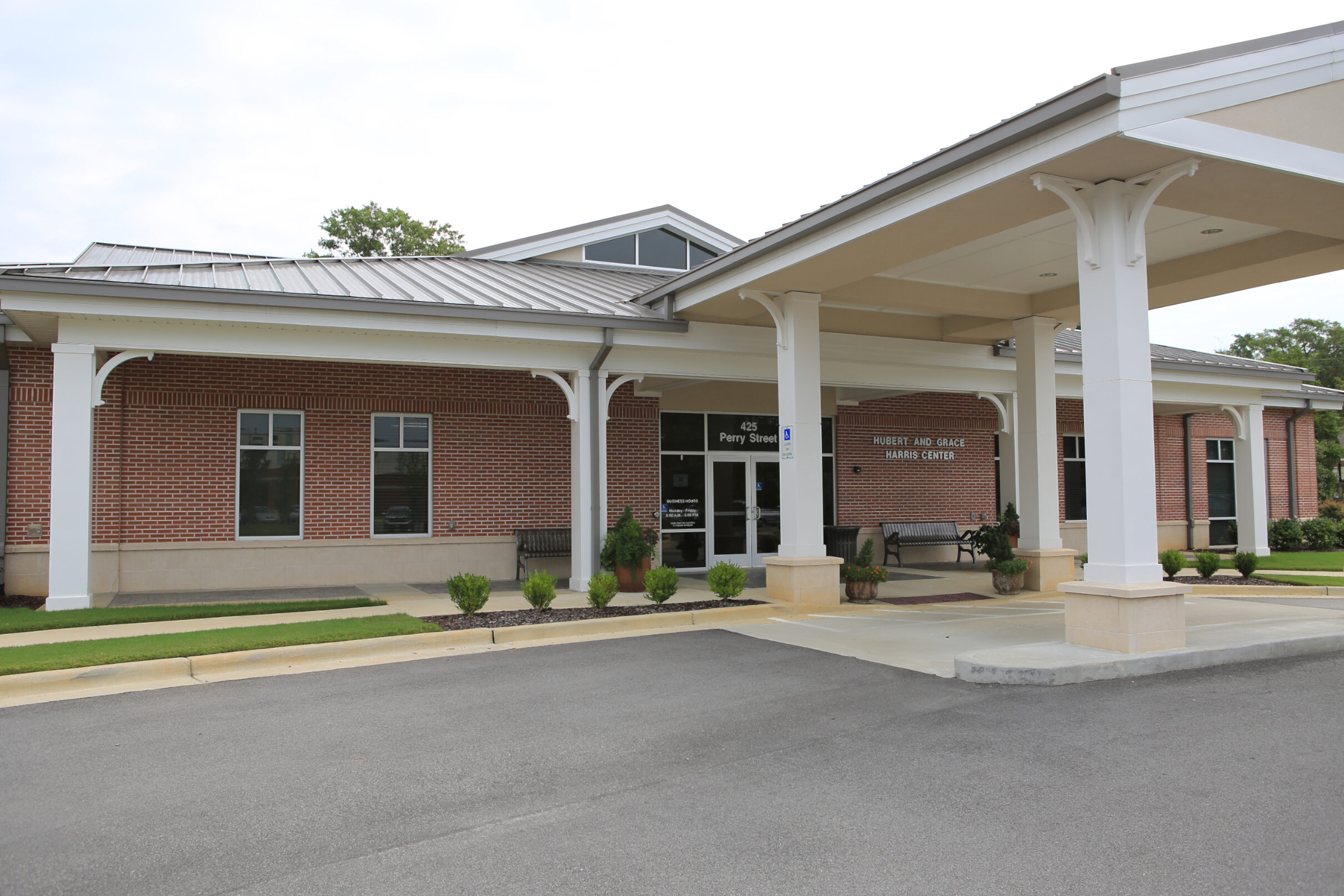 Front entrance of the Hubert and Grace Harris Center, a brick building with a covered drop-off area, columns, and landscaped walkway.