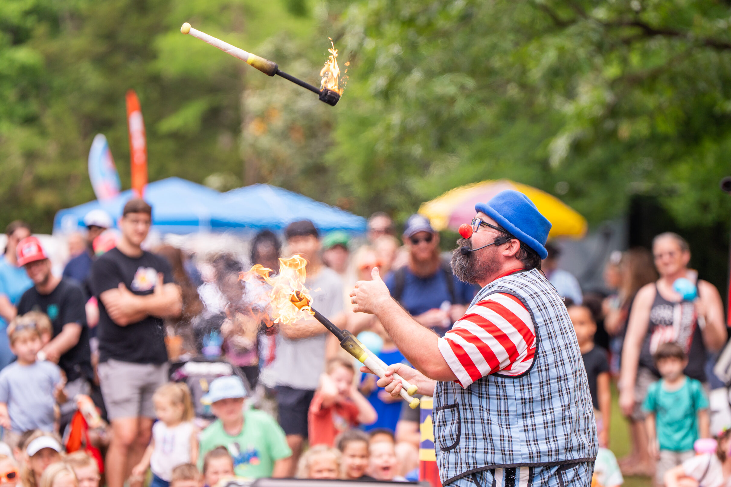 Performer juggling flaming torches at an outdoor event, entertaining a crowd gathered in a park.