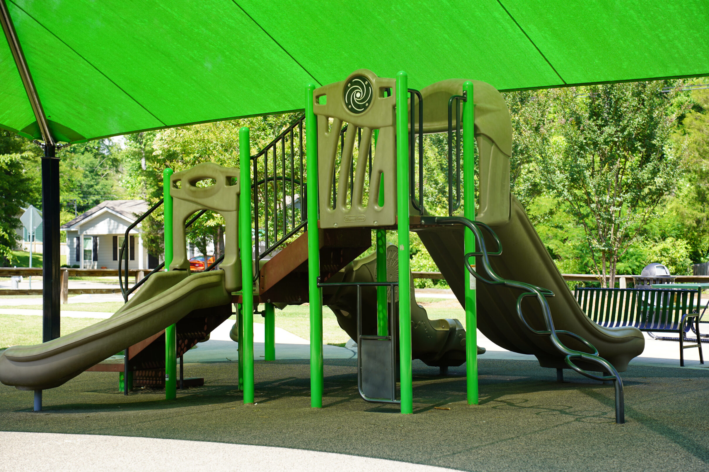 Playground structure on a rubber play area covered by a green pavillion.