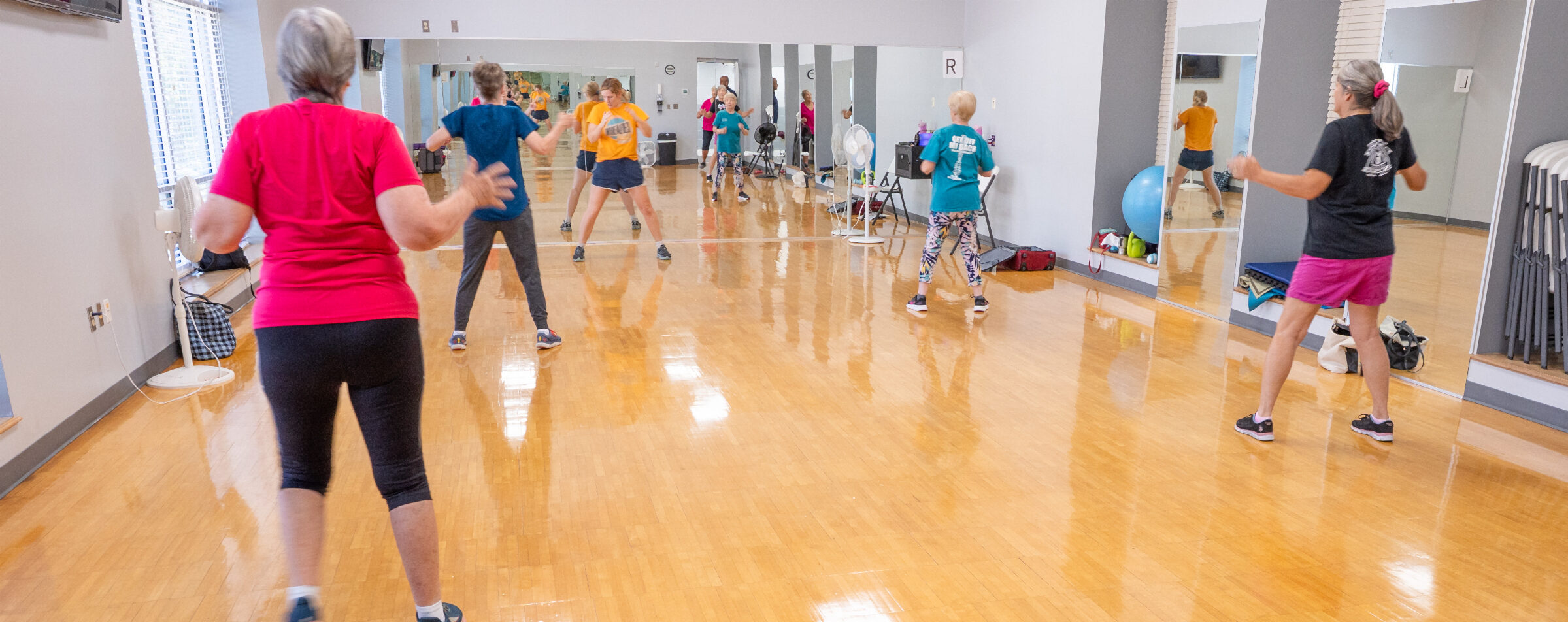A group participating it a fitness class inside a fitness studio with large mirrors and wooden flooring. 