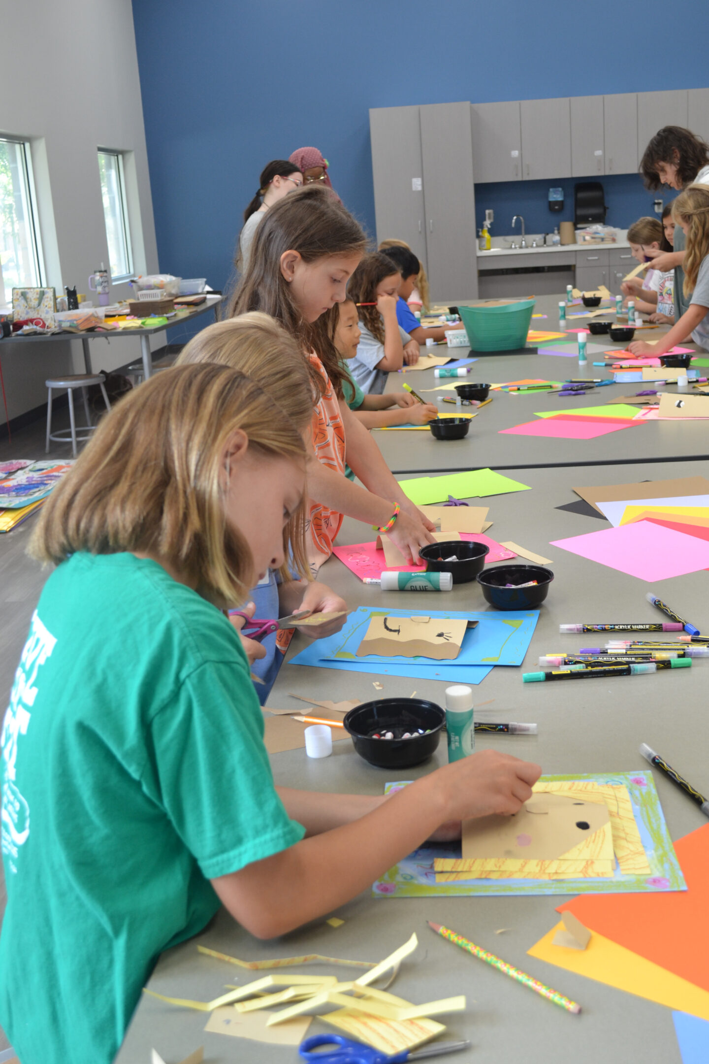 Young girl in green shirt creating an art project at a table.